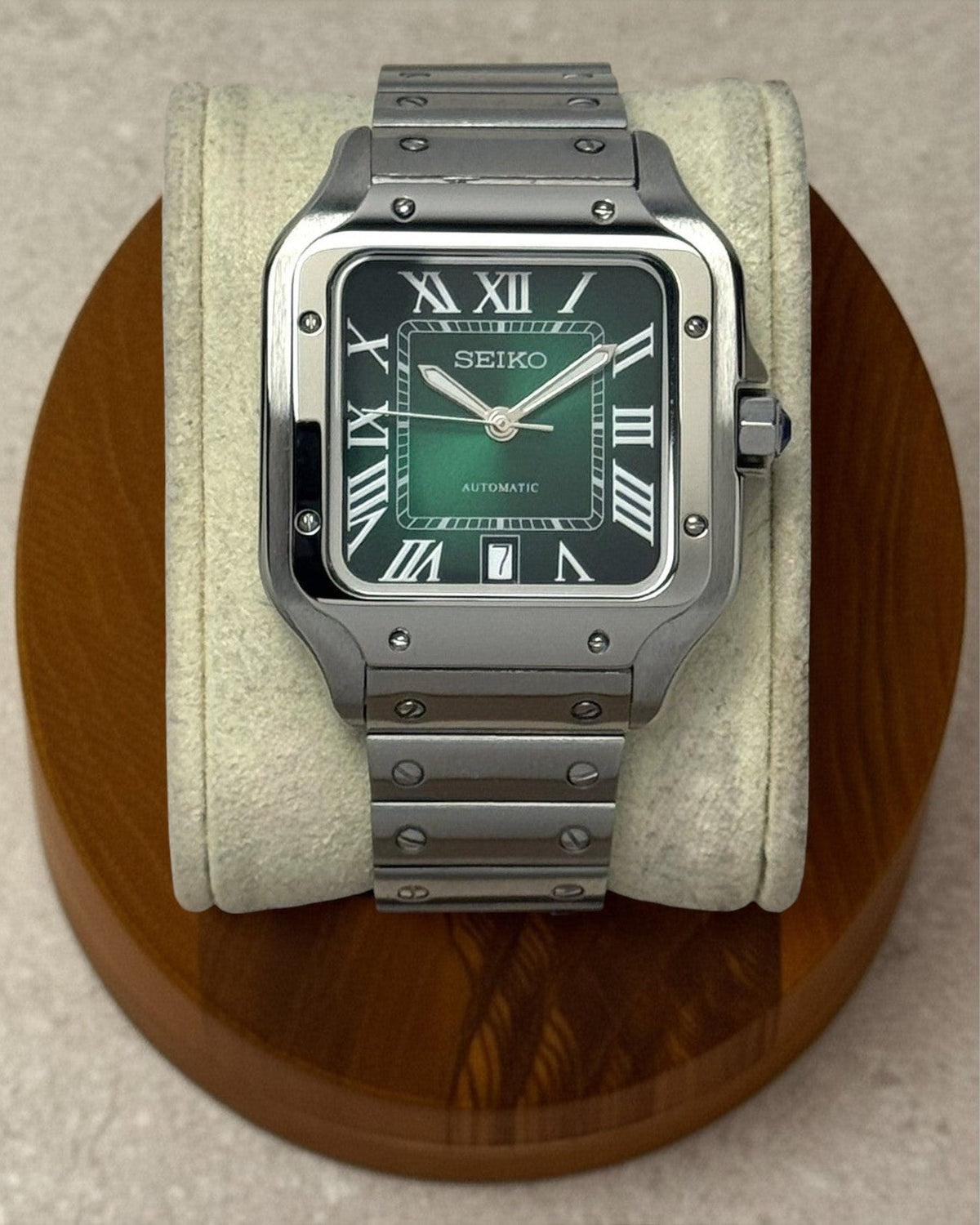 PB TimePiece Aviator watch with a green dial, Roman numerals, and a stainless steel bracelet on a display stand.
