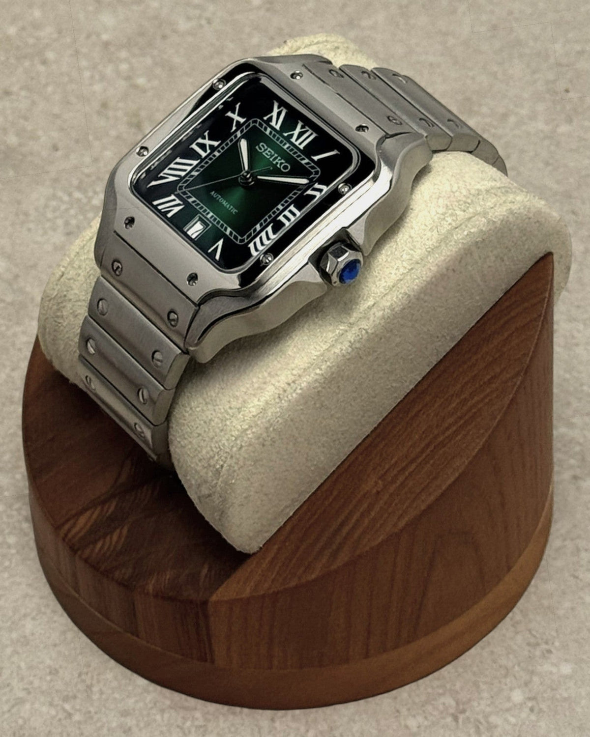 PB TimePiece Aviator watch with a green dial, Roman numerals, and stainless steel bracelet on a wooden display stand.