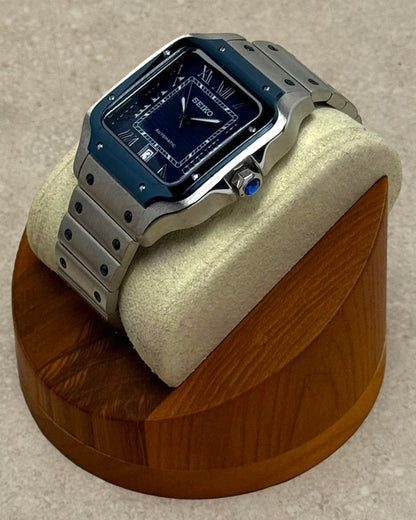 PB TimePiece Aviator watch with a navy blue dial, stainless steel case, and bracelet on a wooden display stand.
