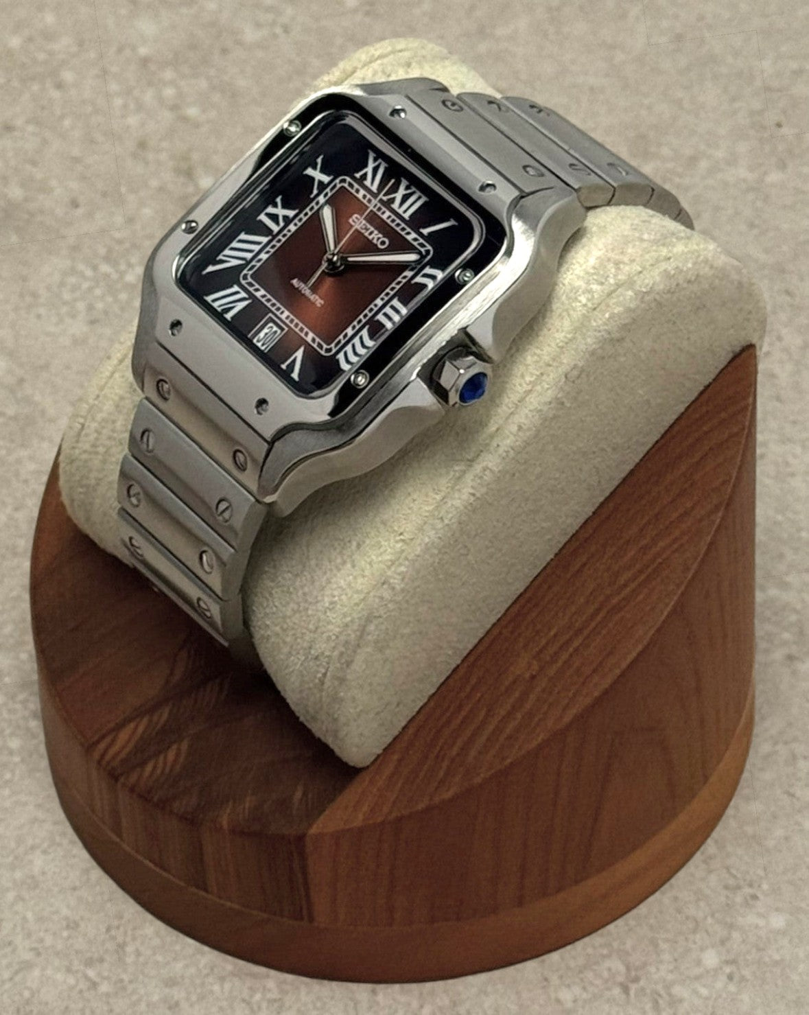 PB TimePiece Aviator watch with ombre brown dial, Roman numerals, and stainless steel bracelet on a display cushion.