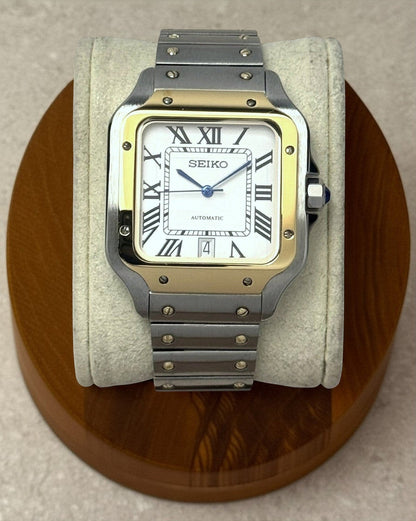 PB TimePiece Aviator watch with a two-tone gold and stainless steel case, white dial, Roman numerals, and blue hands.